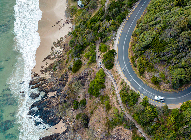 photo from high above of white car driving along a winding coastal road